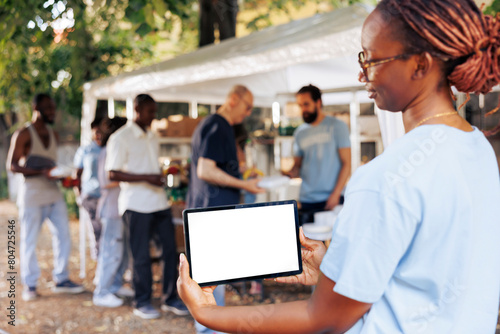 An isolated mockup template for philanthropic messages is held by young black woman holding a digital tablet. African american woman volunteer holding a smart device with a blank white screen display.