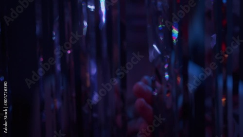 A young woman in the nightclub walks out through silver curtain