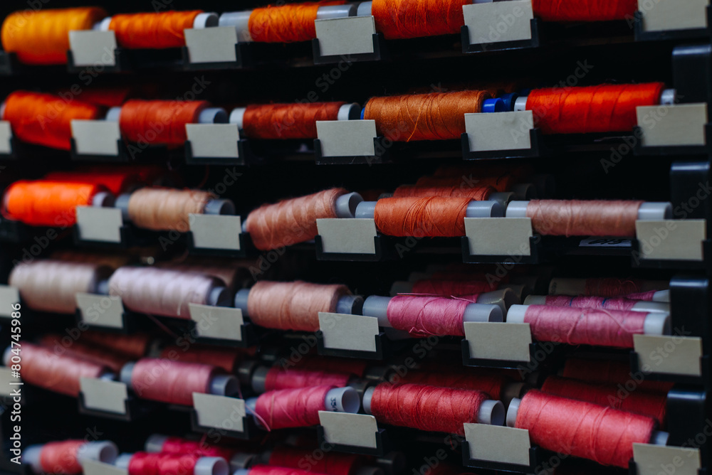 amount of different skeins of threads on special shelves in sewing studio or atelier, several colours, yellow. orange, red and purple, handmade and sewing concept