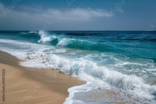 Ocean waves crash onto the shore forming breaks of water. Crashing waves on a sandy beach under a clear blue sky