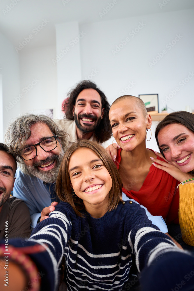 Obraz premium Vertical. Joyful Caucasian family smiling hugging taking a selfie photo indoor. Three generations Caucasian people looking at front camera at home. Happy people relations in domestic life