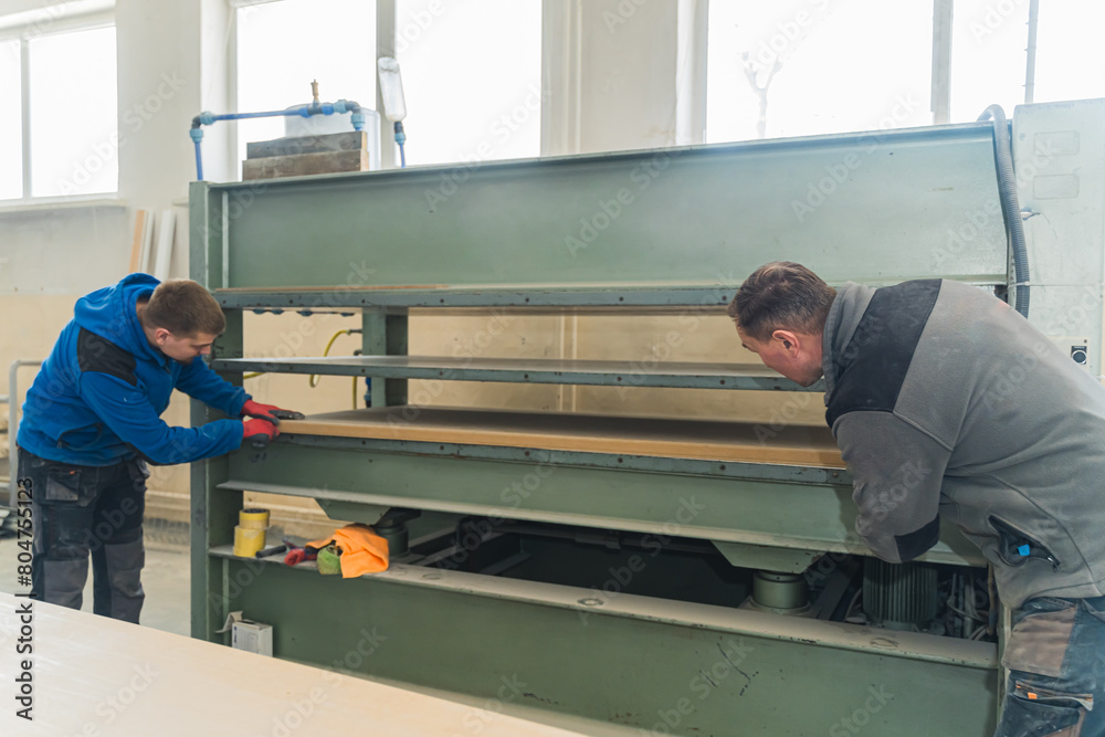 two craftsmen sliding a wide wooden panel in the belt grinder machine. High quality photo two craftsmen sliding a wide wooden panel in the belt grinder machine. High quality photo
