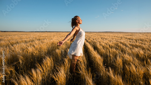 A happy woman in white dress standing in wheat field under blue sky © евгений ставников