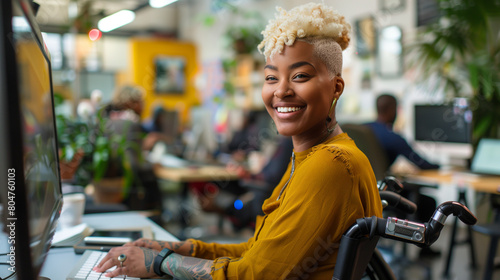 Happy gay african american woman in wheelchair working at computer in an inclusive & diverse office workplace. Disabled black lesbian female with cropped blonde hair collaborating with coworkers photo