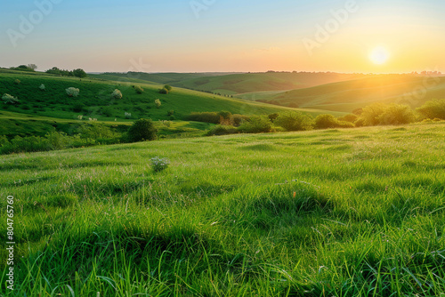 Sunrise over a rolling meadow of green grass  with the distant sound of a morning breeze rustling through scattered trees and bushes.