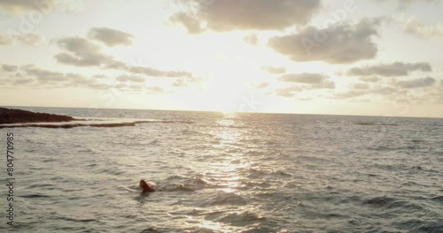 Man paddling on his surfboard in the ocean at sunset aerial