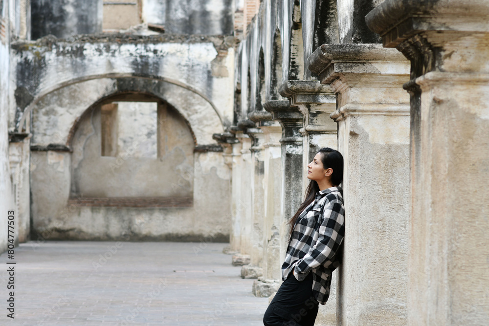 Chica hispana recostada en una columna mientras esta de viaje en Antigua Guatemala. Toma horizontal.