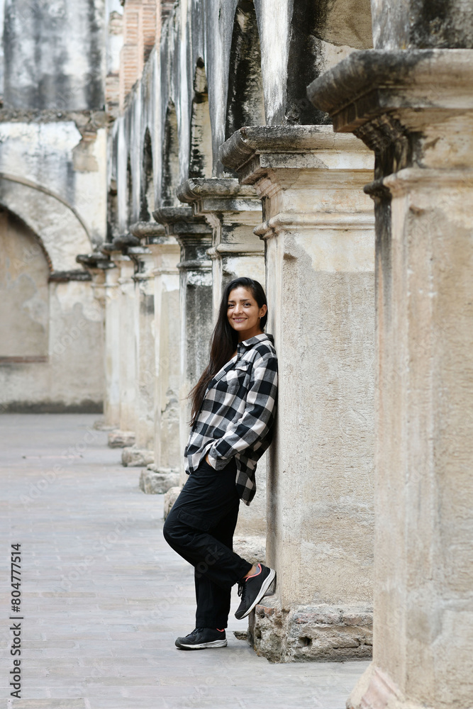 Chica hispana recostada en una columna mientras esta de viaje en Antigua Guatemala. Toma vertical.
