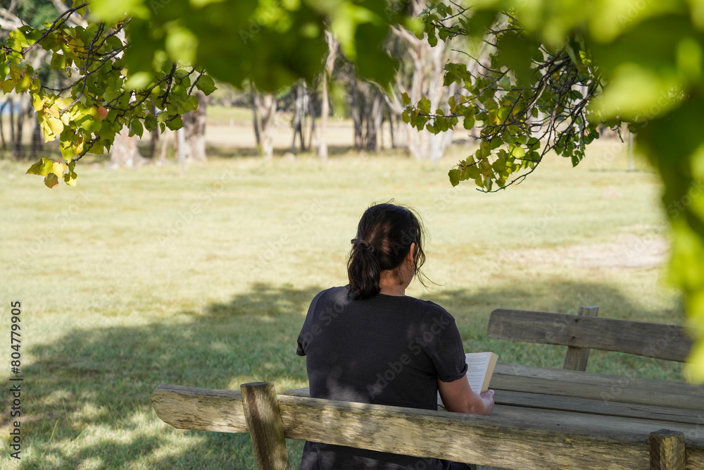 Fototapeta premium Woman reading a book on a wooden bench