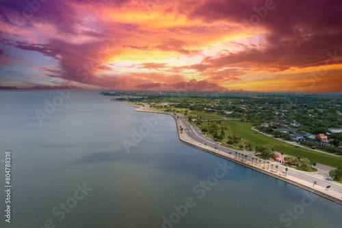 aerial shot along the coast of Lake Pontchartrain with homes, lush green trees, plants and grass, rippling water, powerful clouds at sunset in New Orleans Louisiana USA