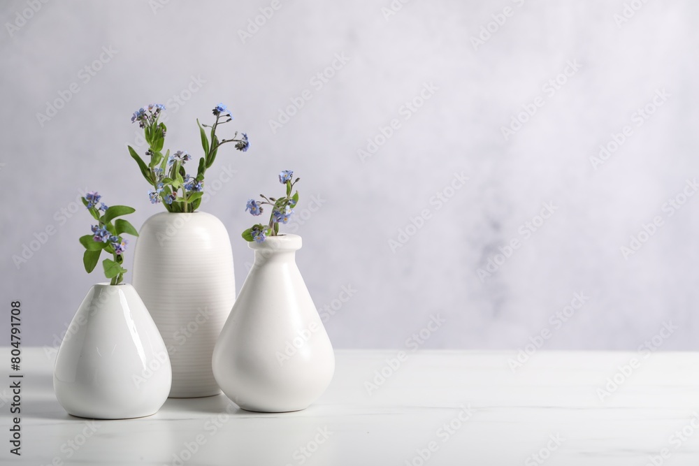 Fototapeta premium Beautiful forget-me-not flowers in vases on white marble table, closeup. Space for text