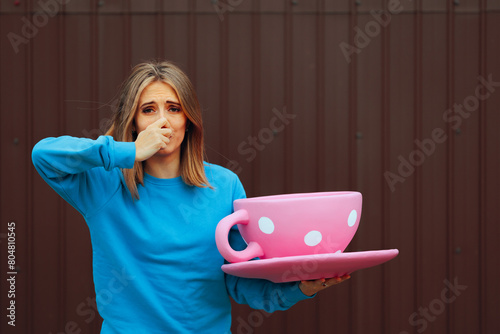 Woman Holding a Huge Cup of Coffee Disliking its Aroma. Unhappy girl feeling unhappy about the smell of caffeine beverage
 photo