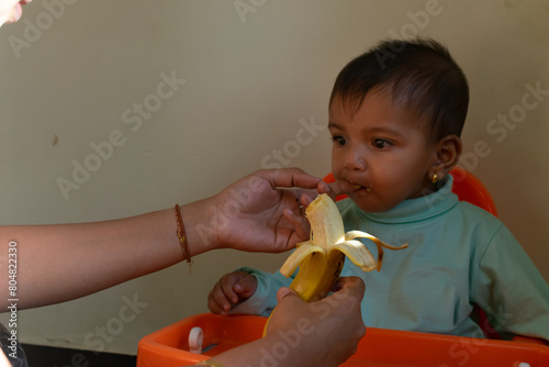 Picture of a baby eating banana. Book, study, learning, focus, chair, feeding tray, table, habit building, development, technology, eyes, addiction, nutrition, stubborn, eat