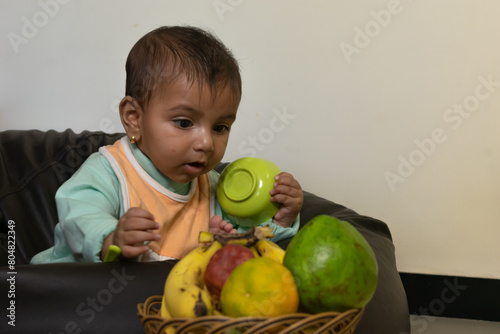 A baby trying to pick fruits. Eating, healthy, bowl, spoon, curious, happy, mother, boy, girl, toddler, kid, game, play, bib, soup, drink, sip, bite, feed, sit, cereal, beanbag, chair, health, weight