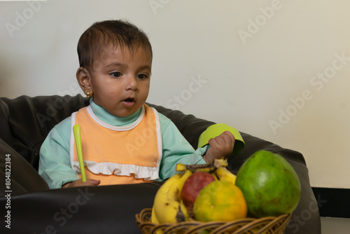 Asian Indian baby boy looking at fruits, eating, spoon bowl feeding mashed boiled teething juice pulp fibre healthy vitamins minerals development growth breakfast chair dine table basket weaning foods