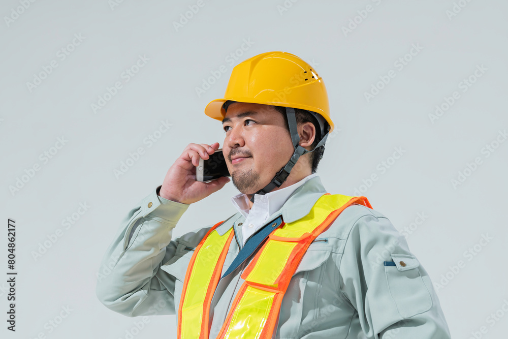 スマートフォンで電話をする作業服の男性 スマートフォンで電話をする作業服の男性