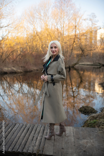 Portrait of a young beautiful blonde girl in a raincoat in the park.