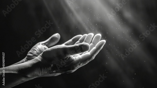 Black and white image capturing dust particles and light rays falling gently upon the outstretched open hands of a person