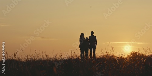 Silhouetted family of four on grassland against warm sunset sky