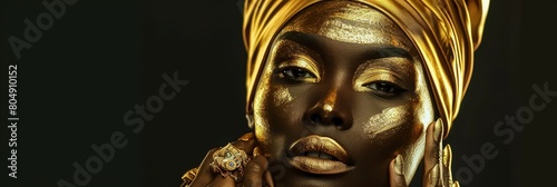 A portrait of an African woman face with golden color on face and jewelry and clothes, hand on face.