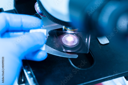 Billede på lærred Scientist wear blue glove holding slide human tissue and out of focus microscope