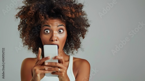Woman is amazed by content she saw or reads shocking message on mobile phone screen. African American woman opens her mouth in surprise and holds her hand. copy space for text. photo