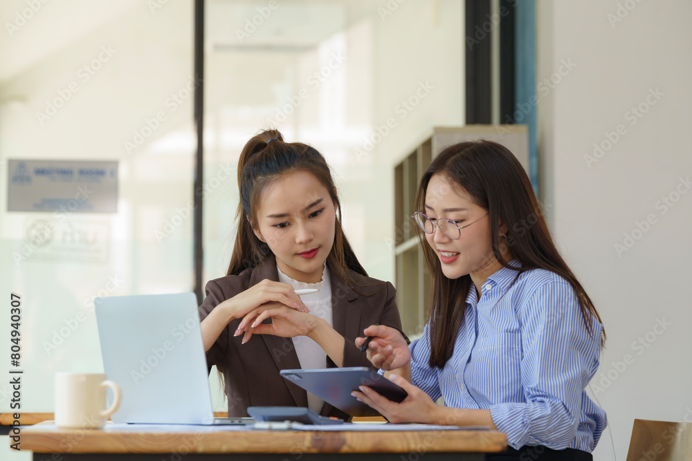 Two Asian businesswomen discuss new startup project idea presentation and analyze planning and financial statistics and investment market at the office. Two Asian businesswomen discuss new startup project idea presentation and analyze planning and financial statistics and investment market at the office.