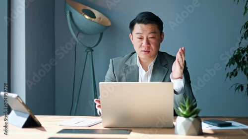 Portrait of successful asian businessman taking part in online conversation through modern portable laptop. Handsome office worker making gesture bye in end on video call. Concept of communication. photo