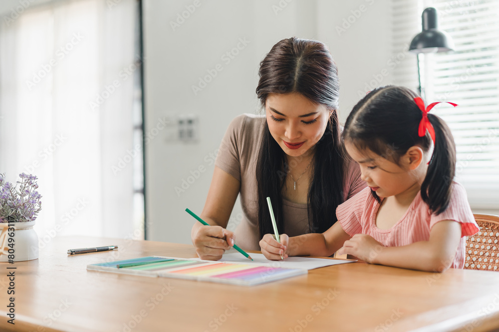 Mother helps daughter doing homework sitting at table writing in paper notebook right answer Mother helps daughter doing homework sitting at table writing in paper notebook right answer