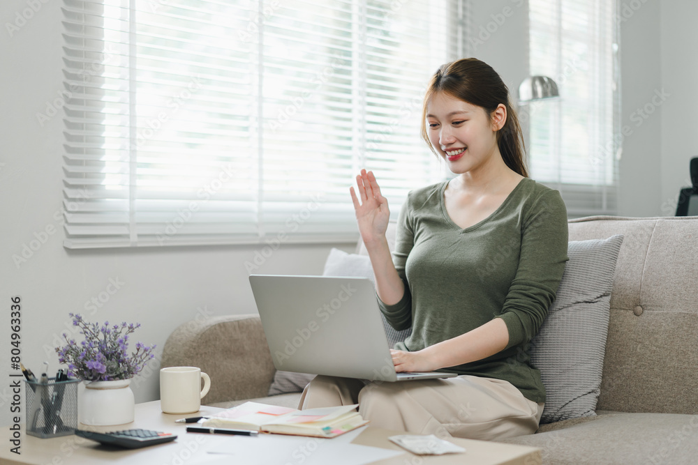 Happy asian woman waving during a video call on laptop at home. Happy asian woman waving during a video call on laptop at home.
