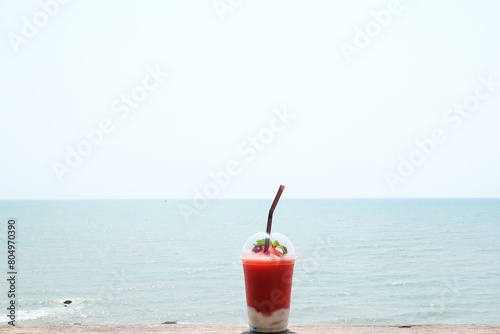 Strawberry yogurt smoothie with strawberry fruit in take away plastic glass on the beach background.