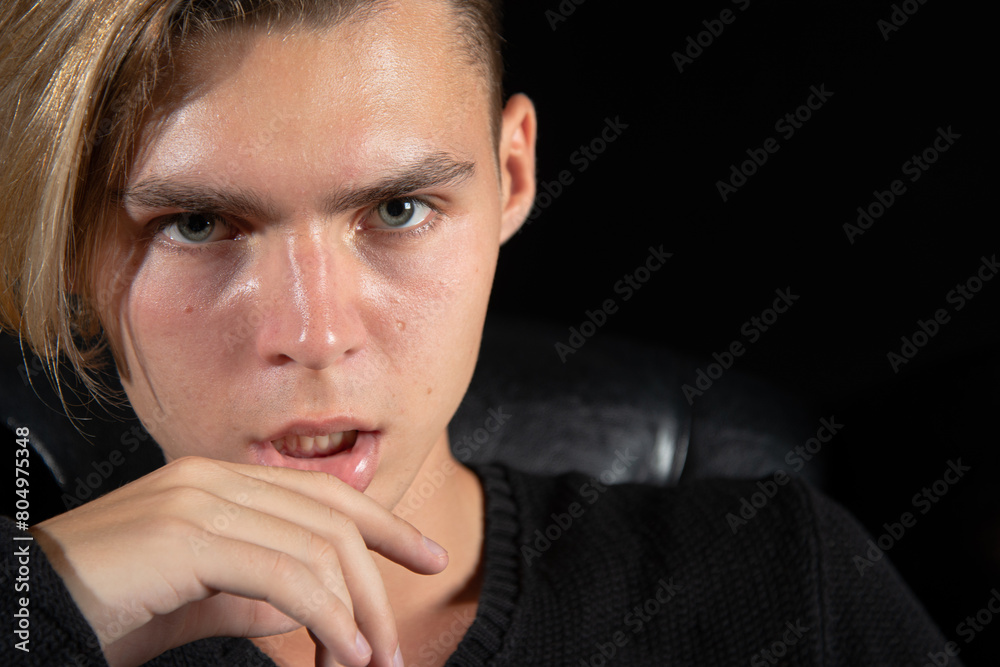 A young attractive guy is sad while sitting on a chair. Black background. A young attractive guy is sad while sitting on a chair. Black background.