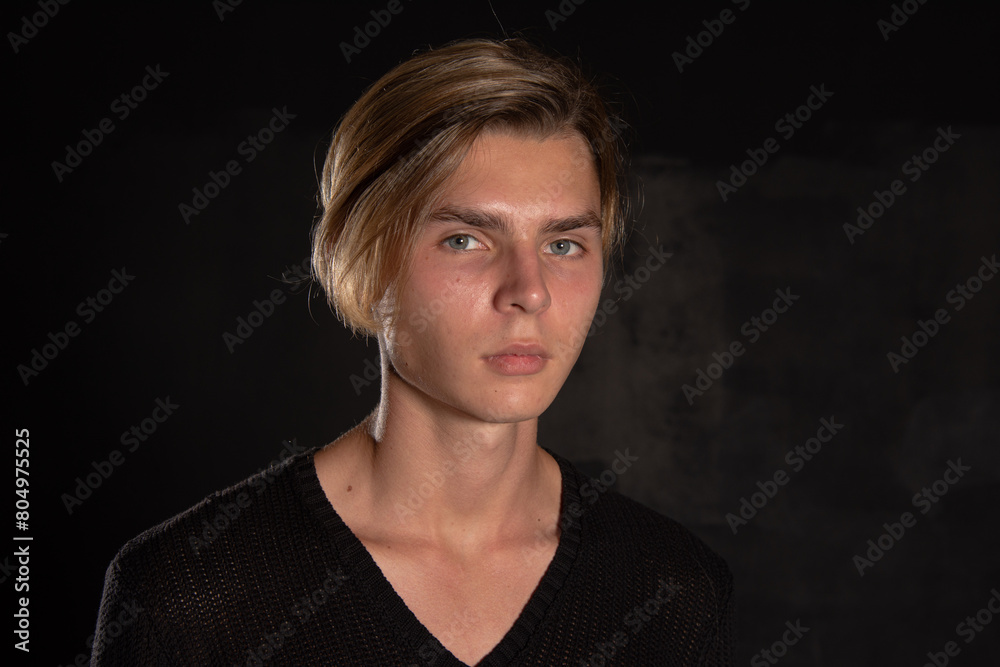 A young attractive guy is sad while sitting on a chair. Black background. A young attractive guy is sad while sitting on a chair. Black background.