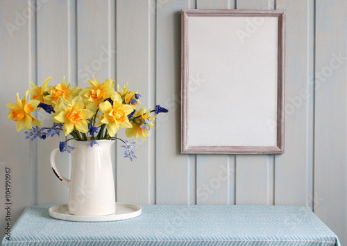 spring mockup. an empty frame on the wall in the cottage and a bouquet of garden flowers in a jug on the table. daffodils and hyacinths.