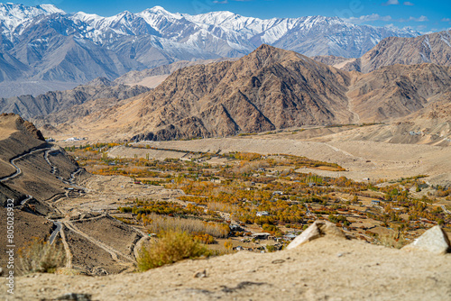 Spectacular high roads wind through rugged mountains beneath blue skies and the remote snow-capped peaks of Ladakh, India.