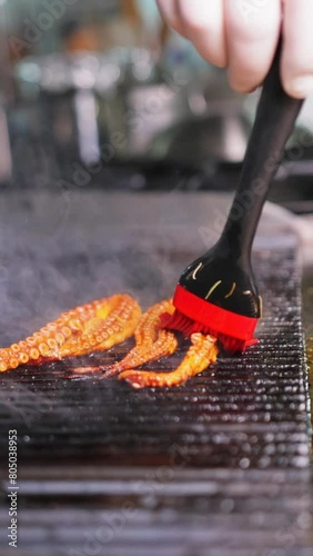Chef brushes sauce onto the octopus on an electric grill using a silicone brush.