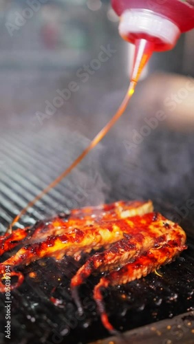 Close-up of chef pours sauce on the grilling octopus on an electric grill in the restaurant kitchen in slow motion. Vertical video format.