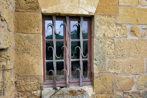 Medieval mullioned window with an ornate wrought iron security grill.
 photo