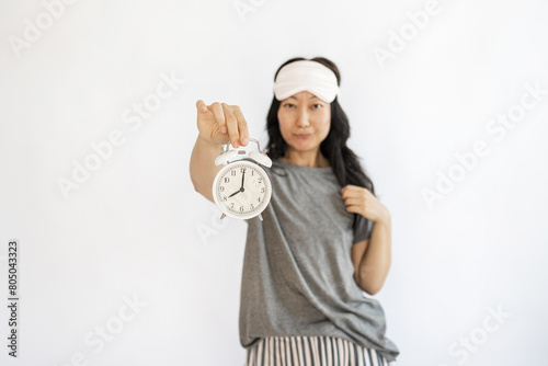 Young Asian woman holding alarm clock on white background with copy space. Good mood night nap concept.