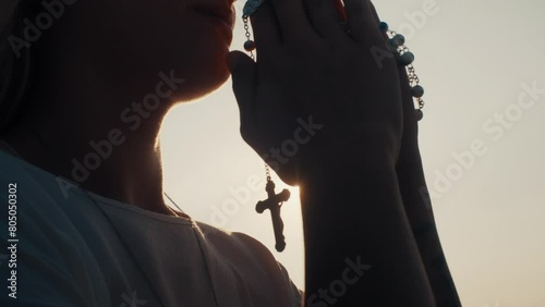 Woman praying while sun shinning through rosary beads