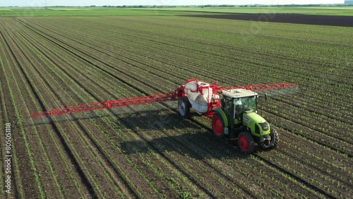 Above view, dolly move around tractor until spraying farmland, dragging mounted wide agricultural sprayer on a field with young new cereal crop, corn, maize.