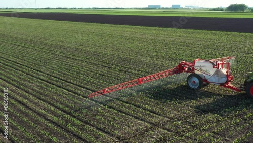 Above view, dolly move around tractor until spraying farmland, dragging mounted wide agricultural sprayer on a field with young new cereal crop, corn, maize.