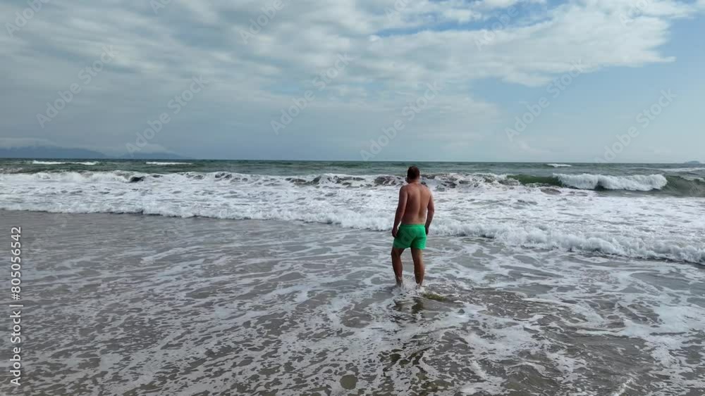 Man in green swim trunks walks on sandy beach with approaching waves, embodying leisure travel and summer vacation concepts Man in green swim trunks walks on sandy beach with approaching waves, embodying leisure travel and summer vacation concepts