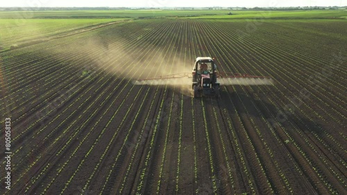 Above view, dolly move with backlight on tractor until spraying farmland, dragging mounted wide agricultural sprayer on a field with young new cereal crop, corn, maize.