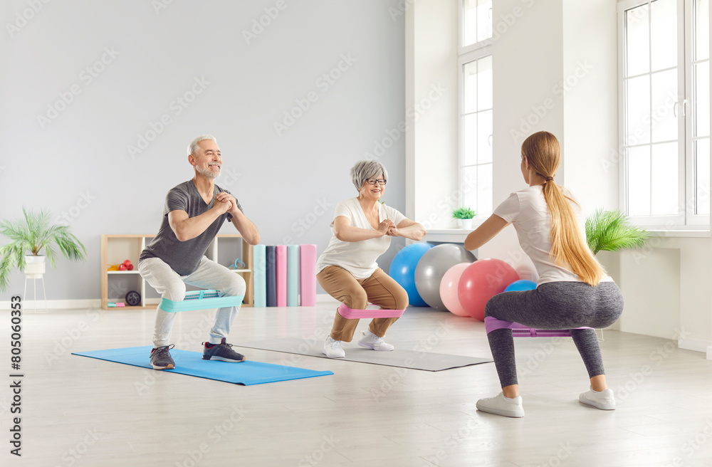 Elderly mature people group exercising with rubber band with fitness trainer in gym. Active seniors having sport workout in a rehab class. Healthy lifestyle and retirement concept.