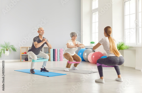 Elderly mature people group exercising with rubber band with fitness trainer in gym. Active seniors having sport workout in a rehab class. Healthy lifestyle and retirement concept.
