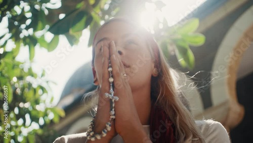 Woman praying with rosary standing under a tree