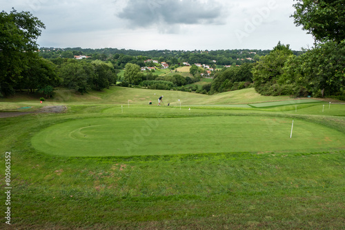 Campo de golfe rodeado por verdes campos a alguma floresta à volta com um golfista ao fundo a treinar as suas habilidades num dia muito nublado photo