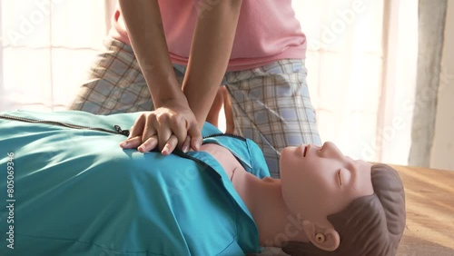 Close-up of young Asian female hands performing cardiopulmonary resuscitation (CPR) on a training dummy. Key elements include defibrillator, compressions, mouth-to-mouth, and abdominal thrusts. photo