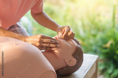 Close-up of young Asian female hands performing cardiopulmonary resuscitation (CPR) on a training dummy. Key elements include defibrillator, compressions, mouth-to-mouth, and abdominal thrusts. photo